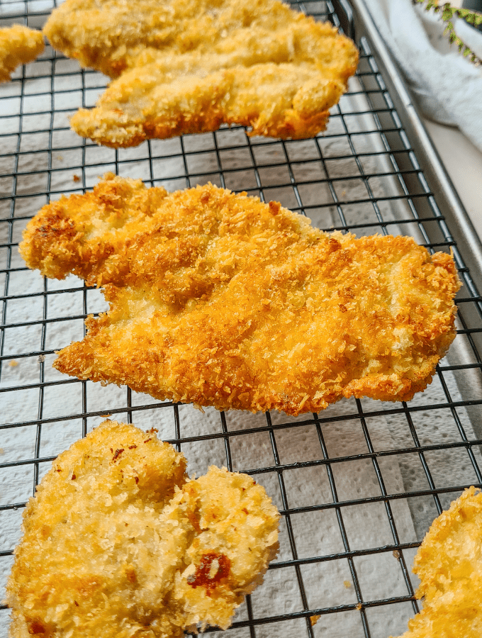 close up of golden crispy panko chicken schnitzel pieces sat on a cooling rack