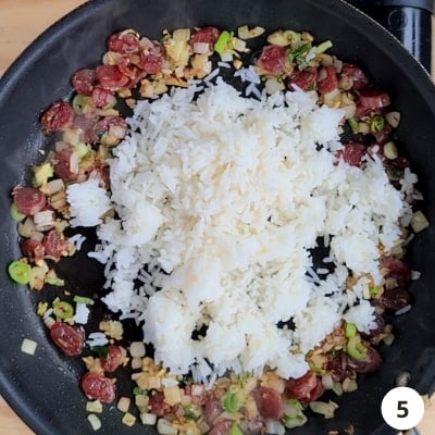 White rice poured into the centre of pan with sausages and onions pushed to the sides of pan