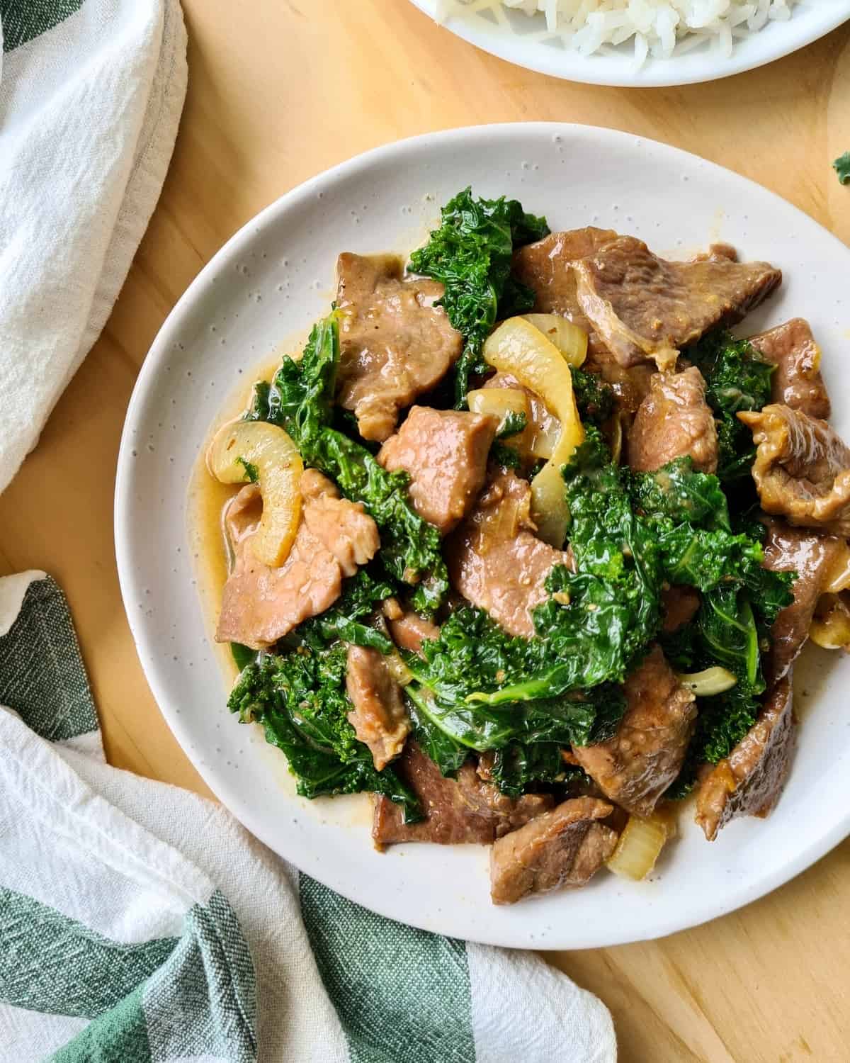 A large plate of ginger beef and kale with table cloth loosely place on its left