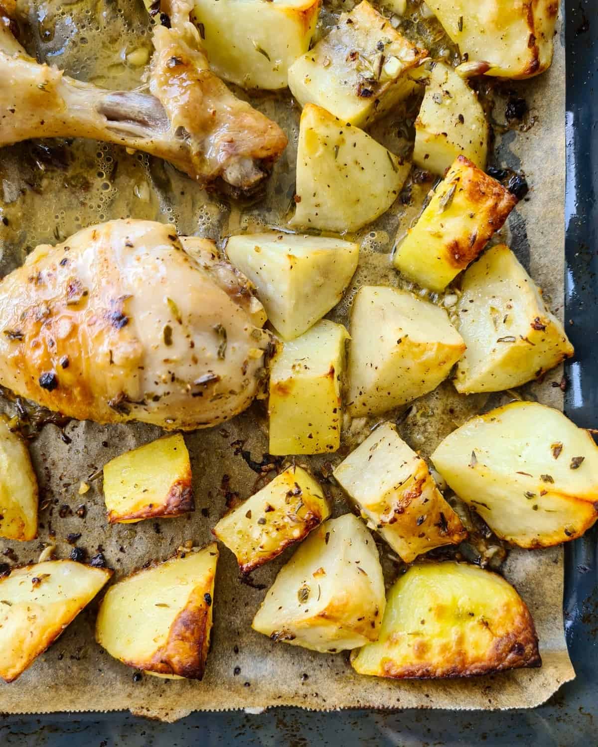 close up image of a corner of a baking tray filled with roasted potatoes and drumsticks