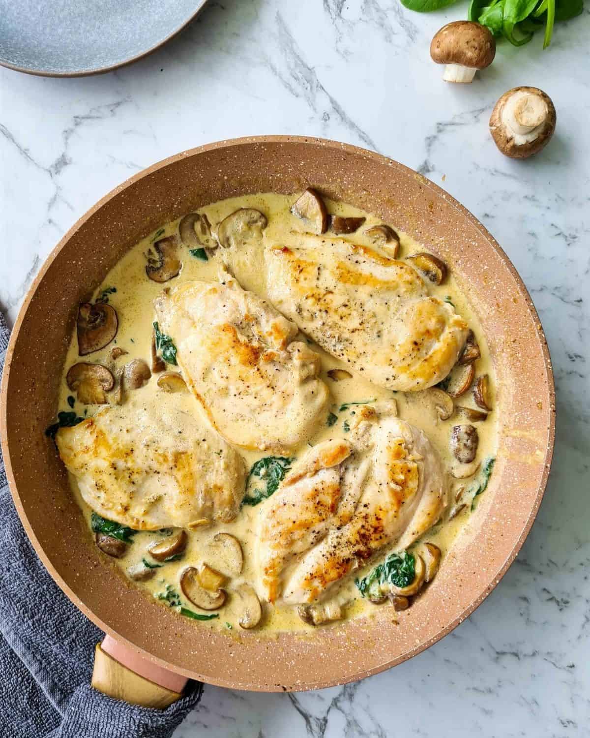 A pan of chicken breasts with creamy mushrooms and spinach straight off the stove