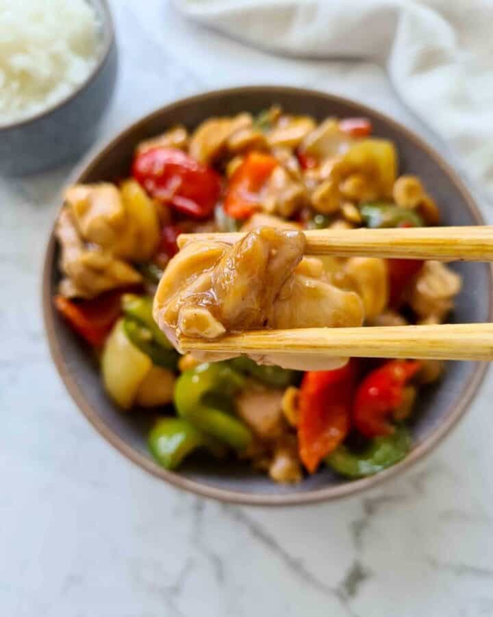 Close up piece of glazed coated chicken held up by a pair of chopsticks