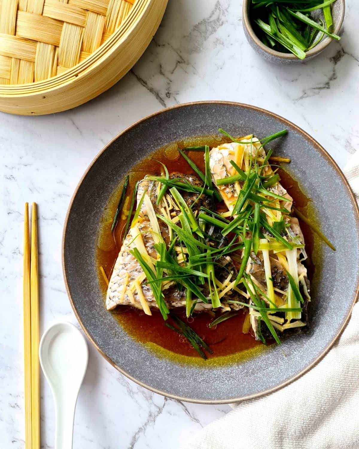 Overhead view of a plate of cooked steamed barramundi topped with lots of ginger and fresh spring onions 