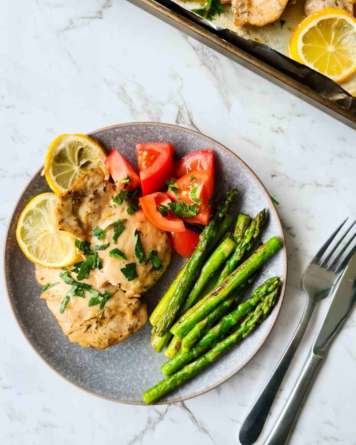 A plate of a simple and healthy dinner with these chicken thighs, asparagus and some tomatoes