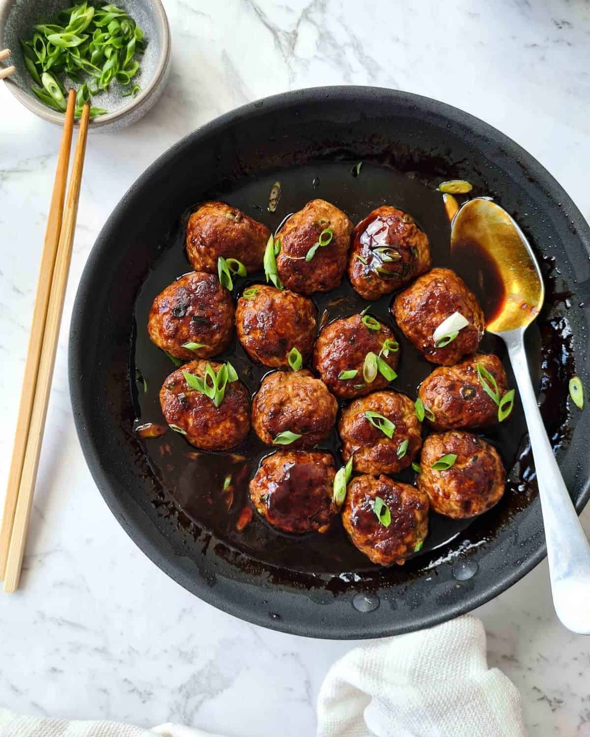 Freshly cooked Asian pork meatballs in a skillet, sprinkled with finely sliced spring onions 