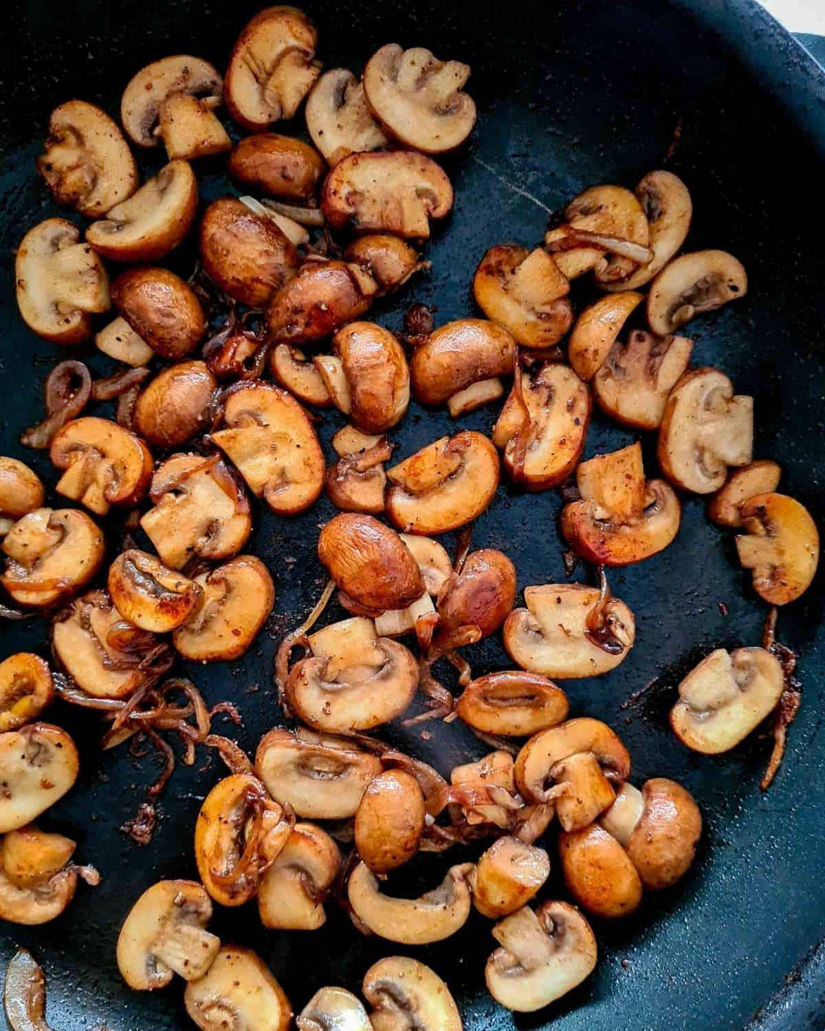 Close up of caramelised mushroom slices and onions in a black pan
