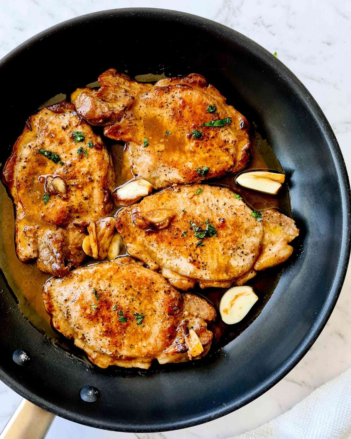 Overhead view of 4 cooked pork chops covered in garlic butter sauce in a black pan