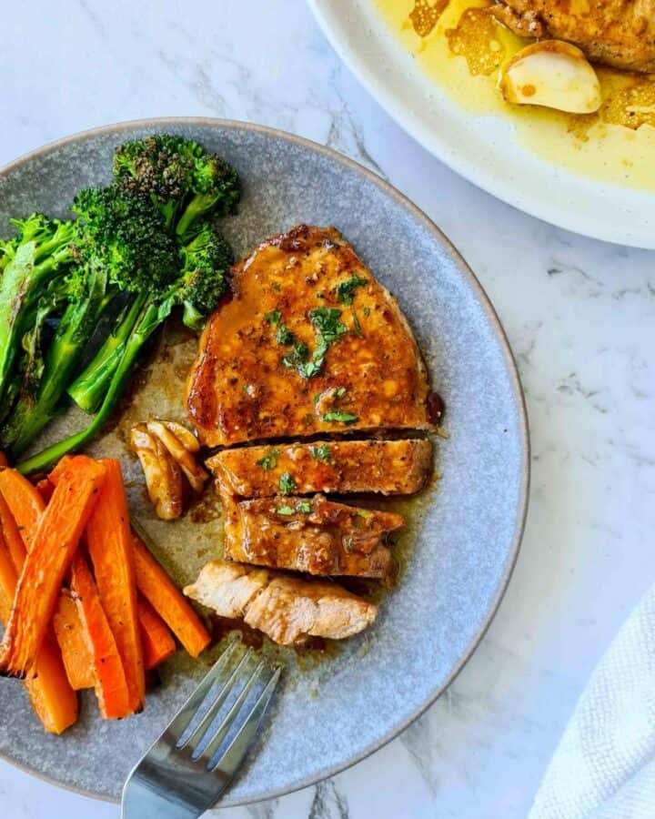 Pork chop on a serving dish, thickly cut to bite size with a side of grilled carrots sticks and broccolini