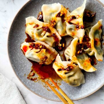 Close up of a plate of boiled dumplings drizzled in chilli oil dipping sauce