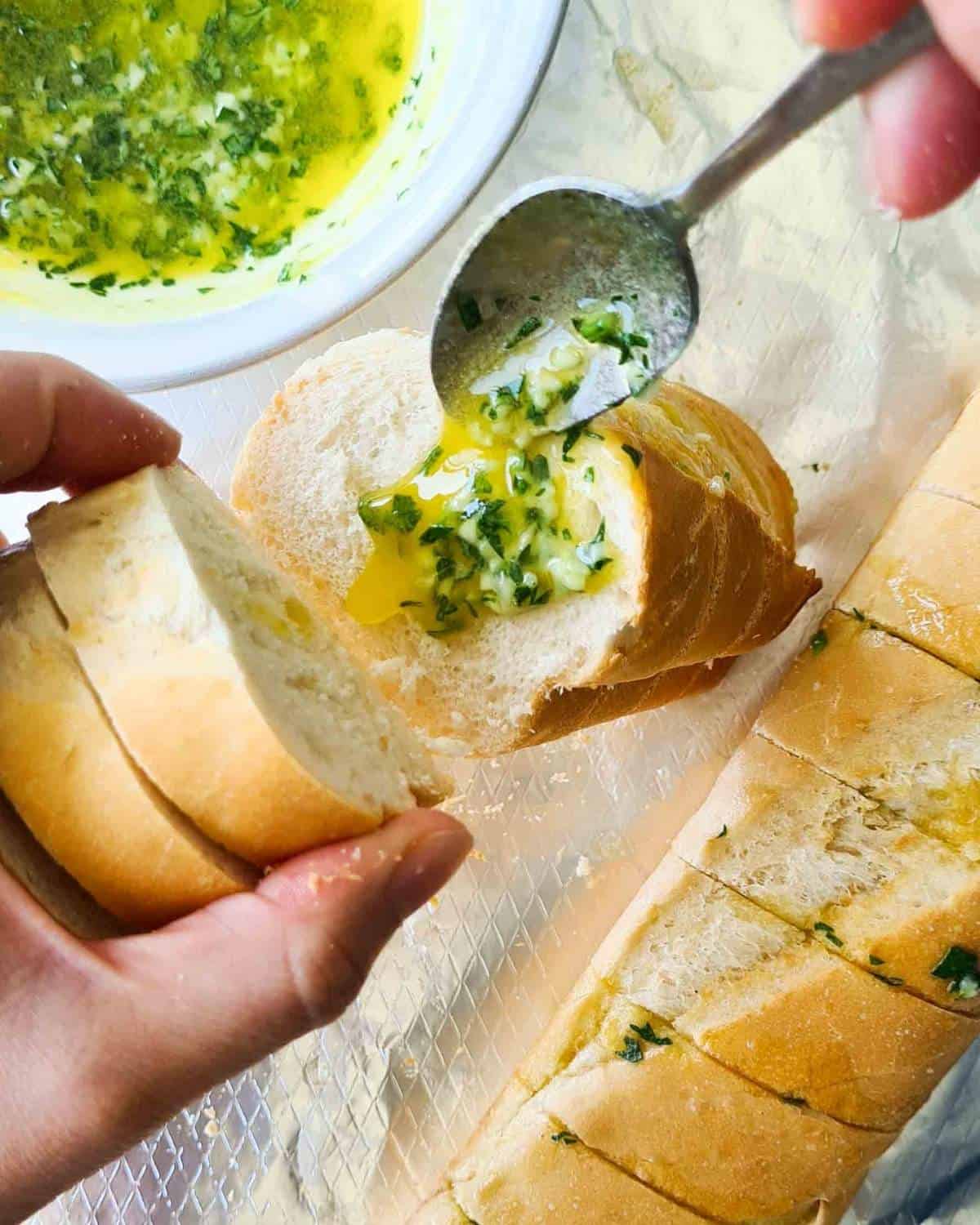 Melted garlic butter being spooned onto a cut side of a baguette