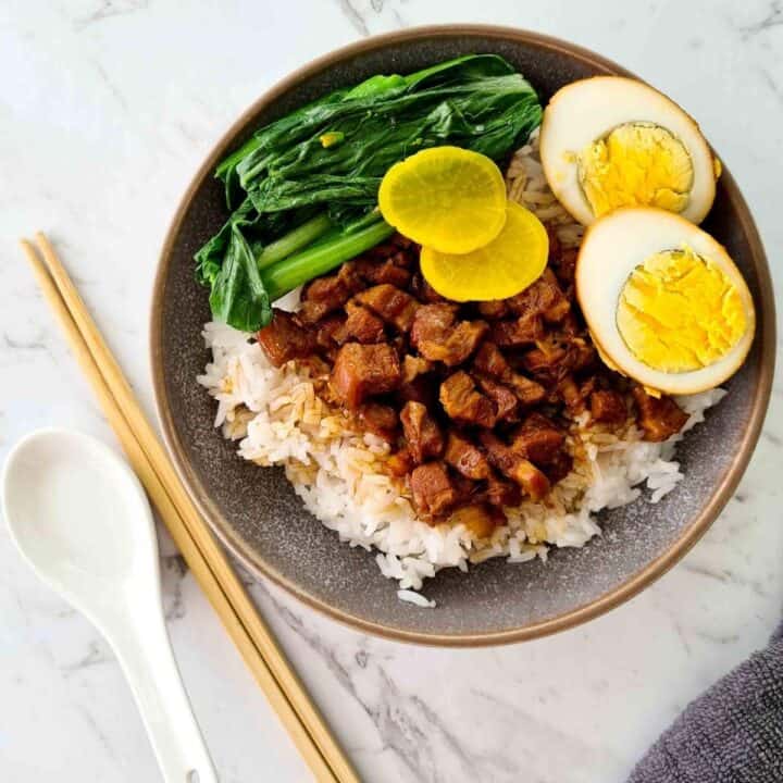 A bowl of rice topped with braised pork, vegetables and an egg