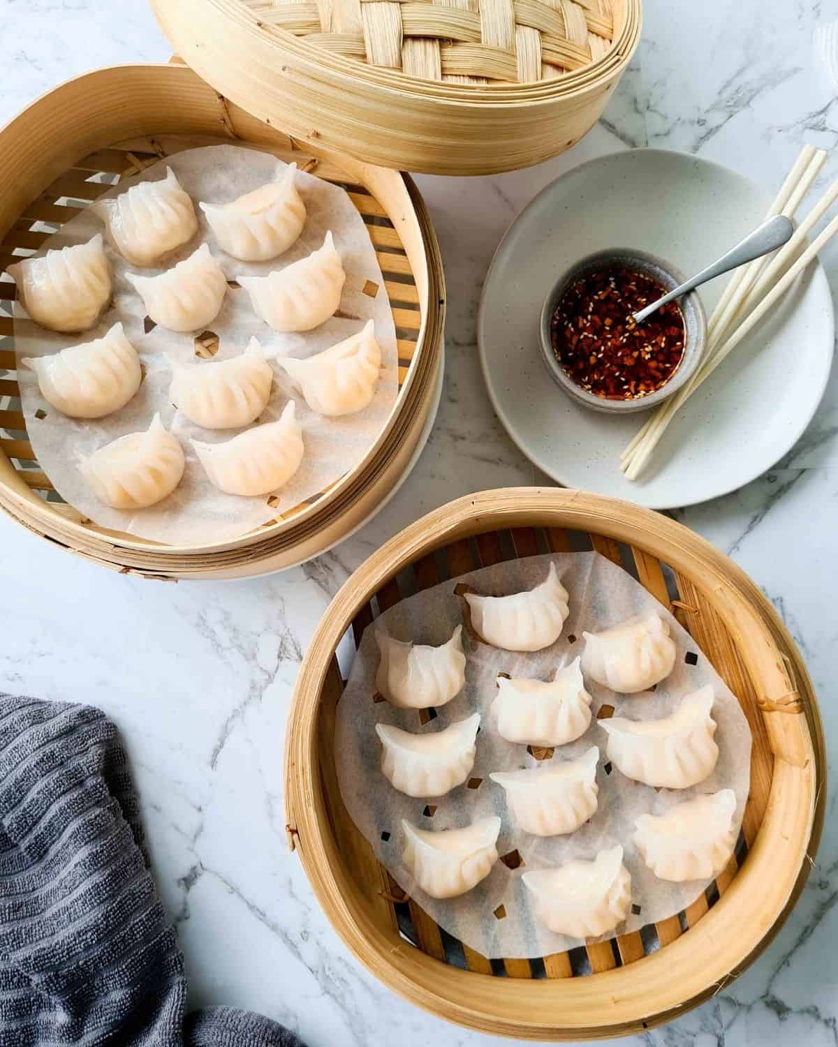 Two baskets filled with cooked dumplings with a side of dipping sauce