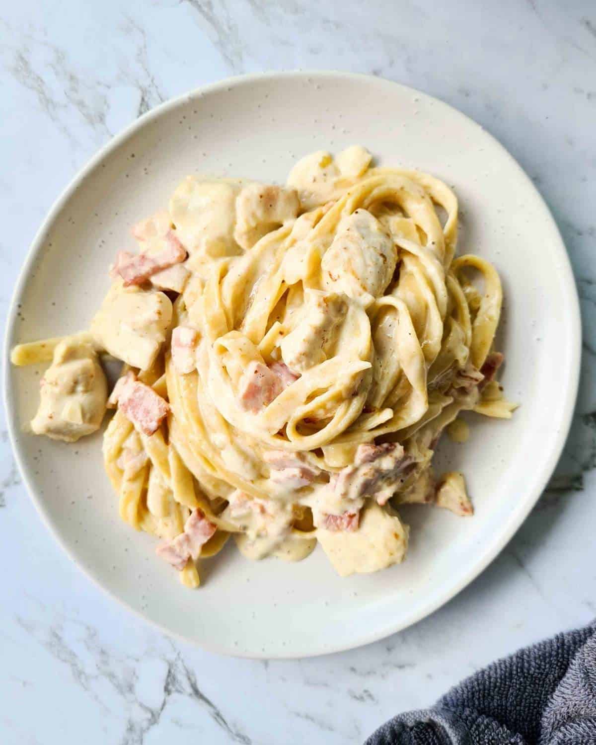 Creamy pasta with chicken and bacon pieces on a white plate