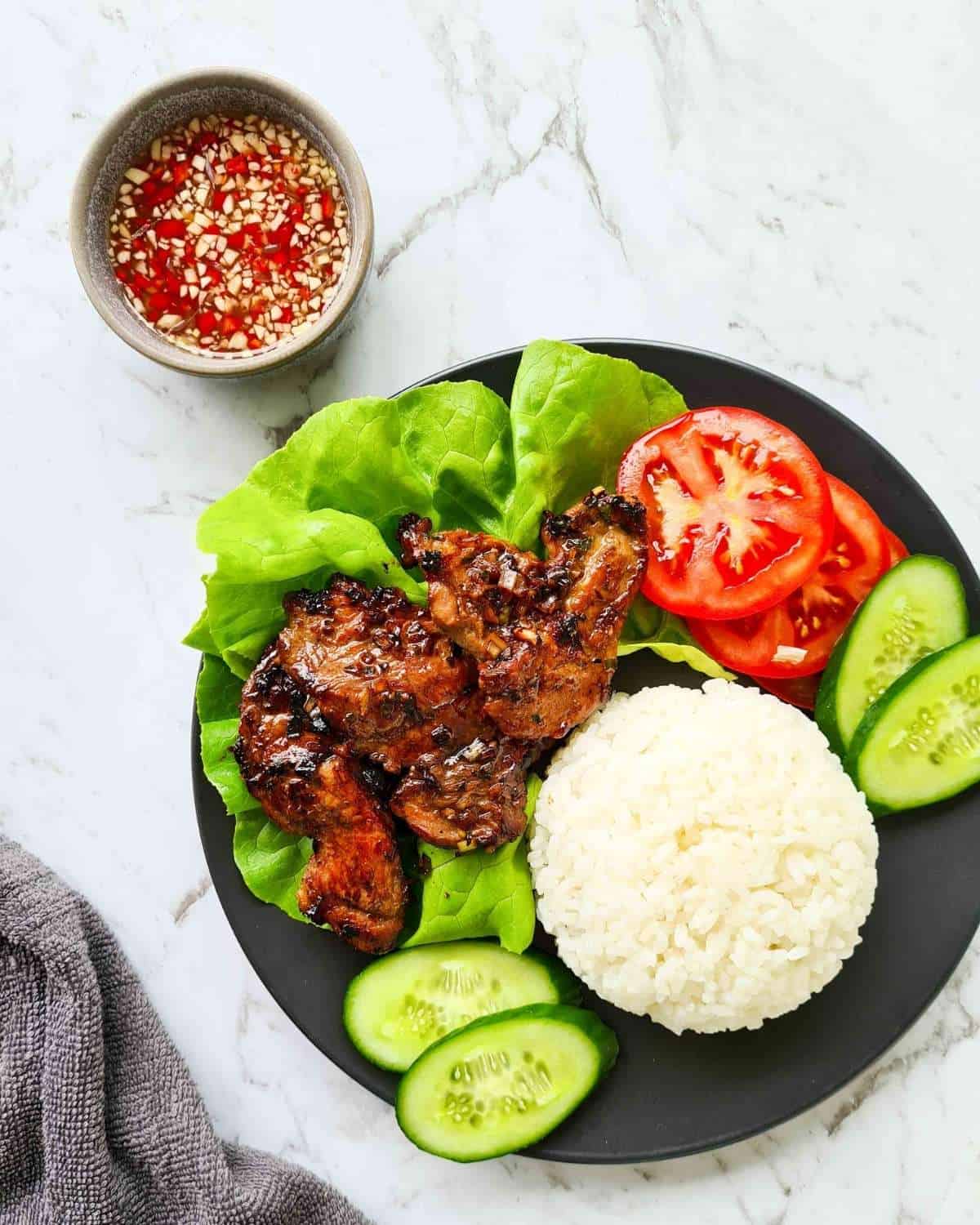 A plate of Vietnamese pork and rice with a side of dipping sauce
