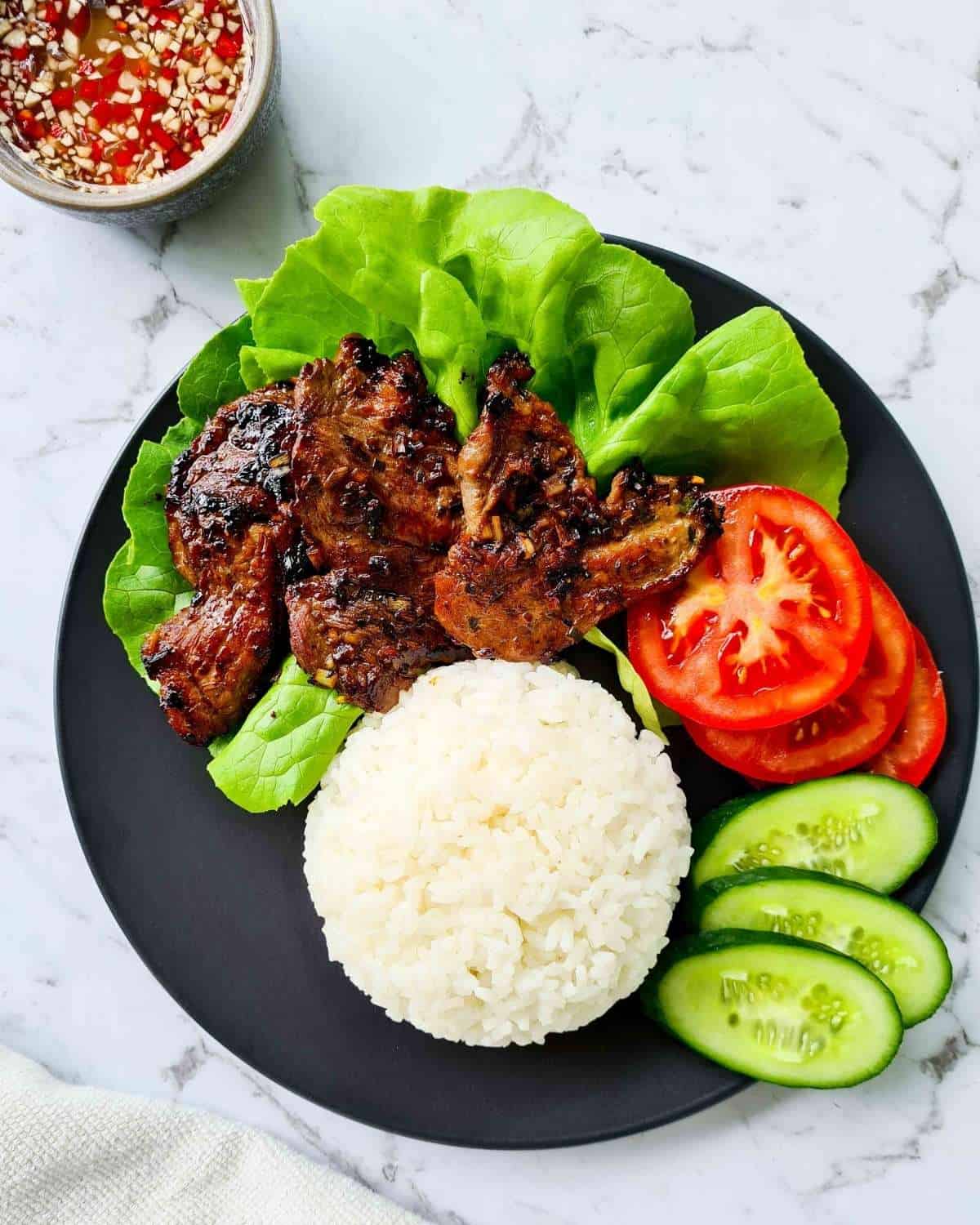 Lightly charred pork with rice, fresh tomatoes and cucumber slices on a black plate
