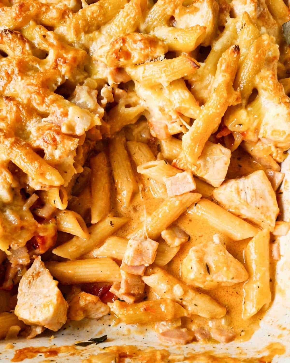 Close up of a tray of creamy pasta bake with a few scoops taken out of the tray