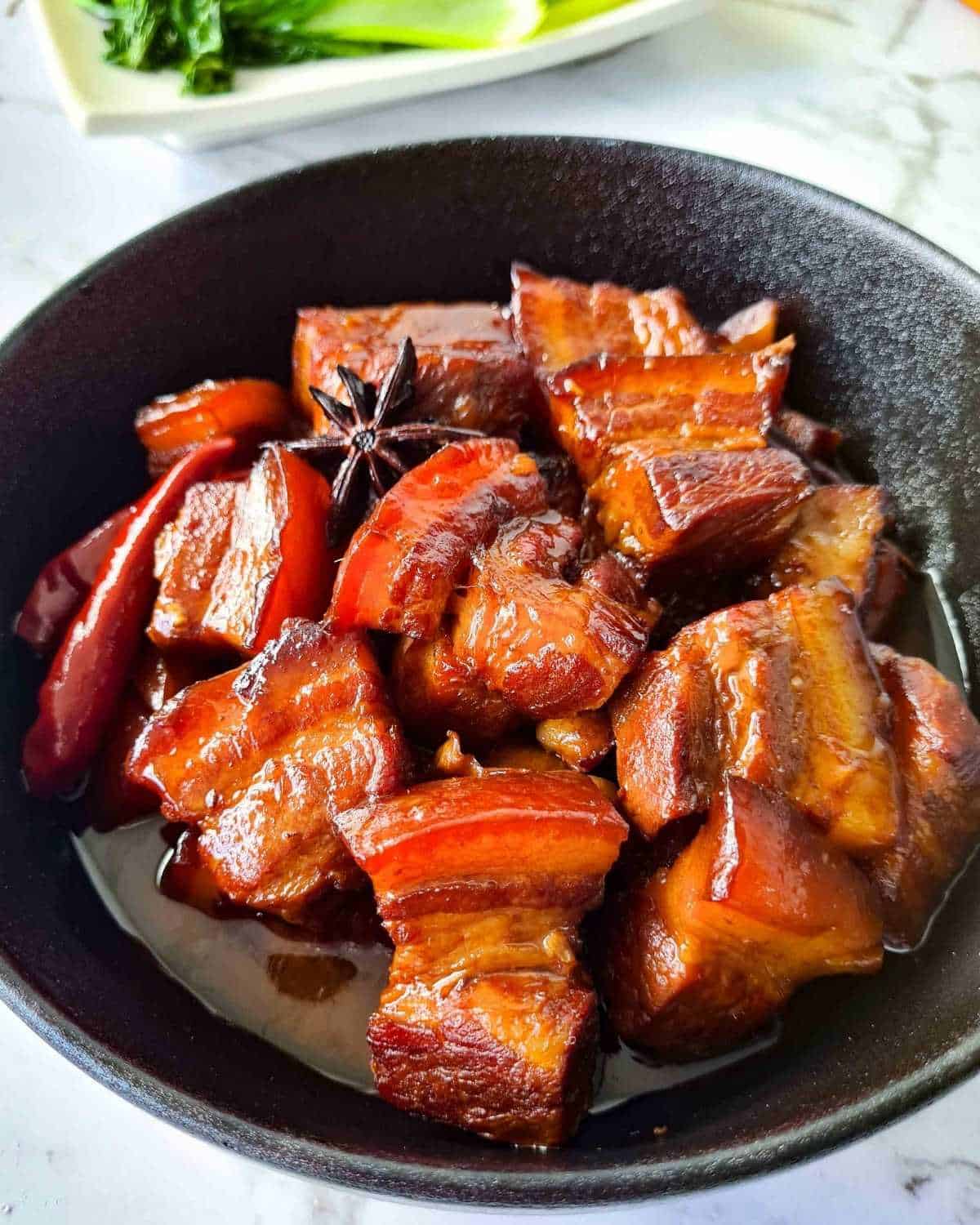 Close up of a bowl of red braised pork belly with plenty of glossy sauce