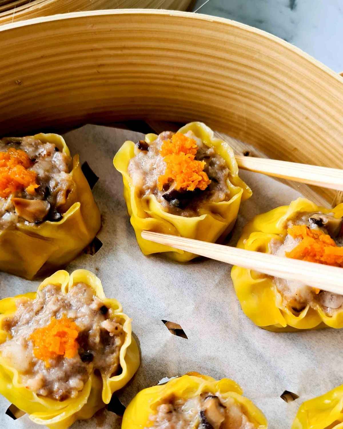 Close up of a siu mai being picked up by a pair of chopsticks inside a steamer