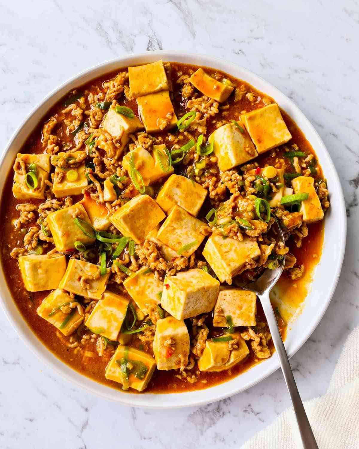 A large plate of mapo tofu with a spoon