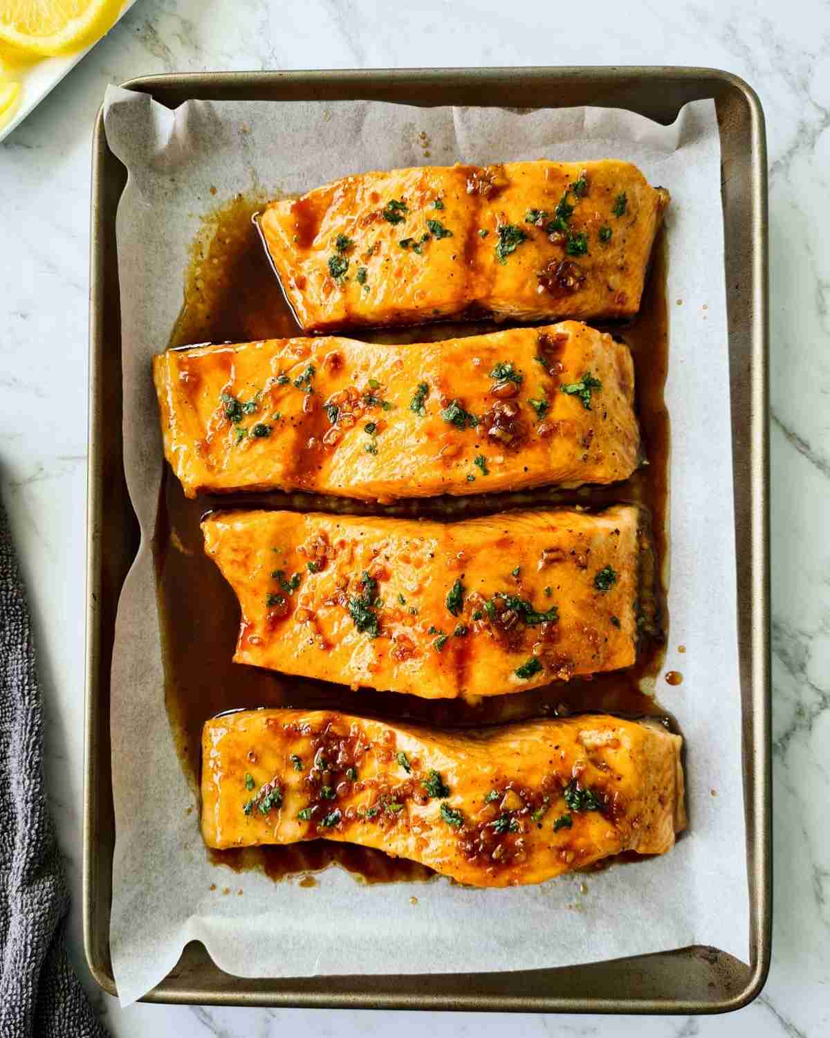 4 cooked salmon fillets in a baking tray with sauce