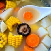 Close up of clear bone soup with corn, skiitake mushrooms, carrots and white radish