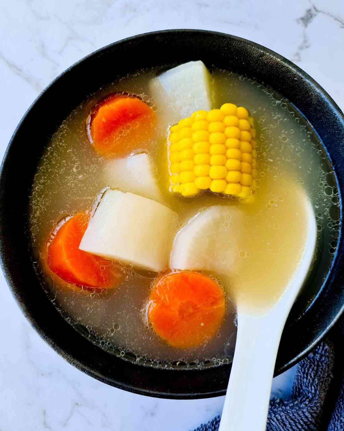 A bowl of bone broth with carrots, white radish and corn kernel