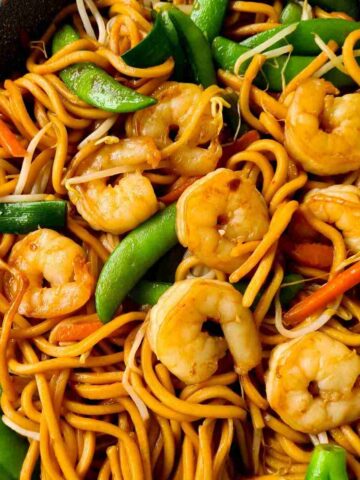 Close up of Hokkien noodles held up by a pair of chopsticks with prawns and vegetables