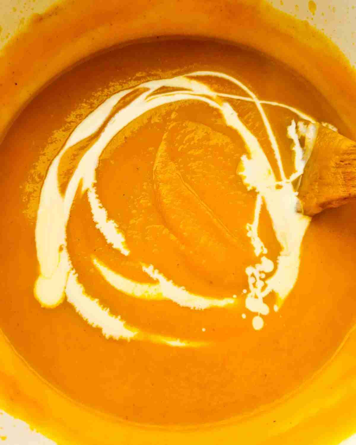 Close up of a pot of pumpkin and sweet potato soup drizzled with cream