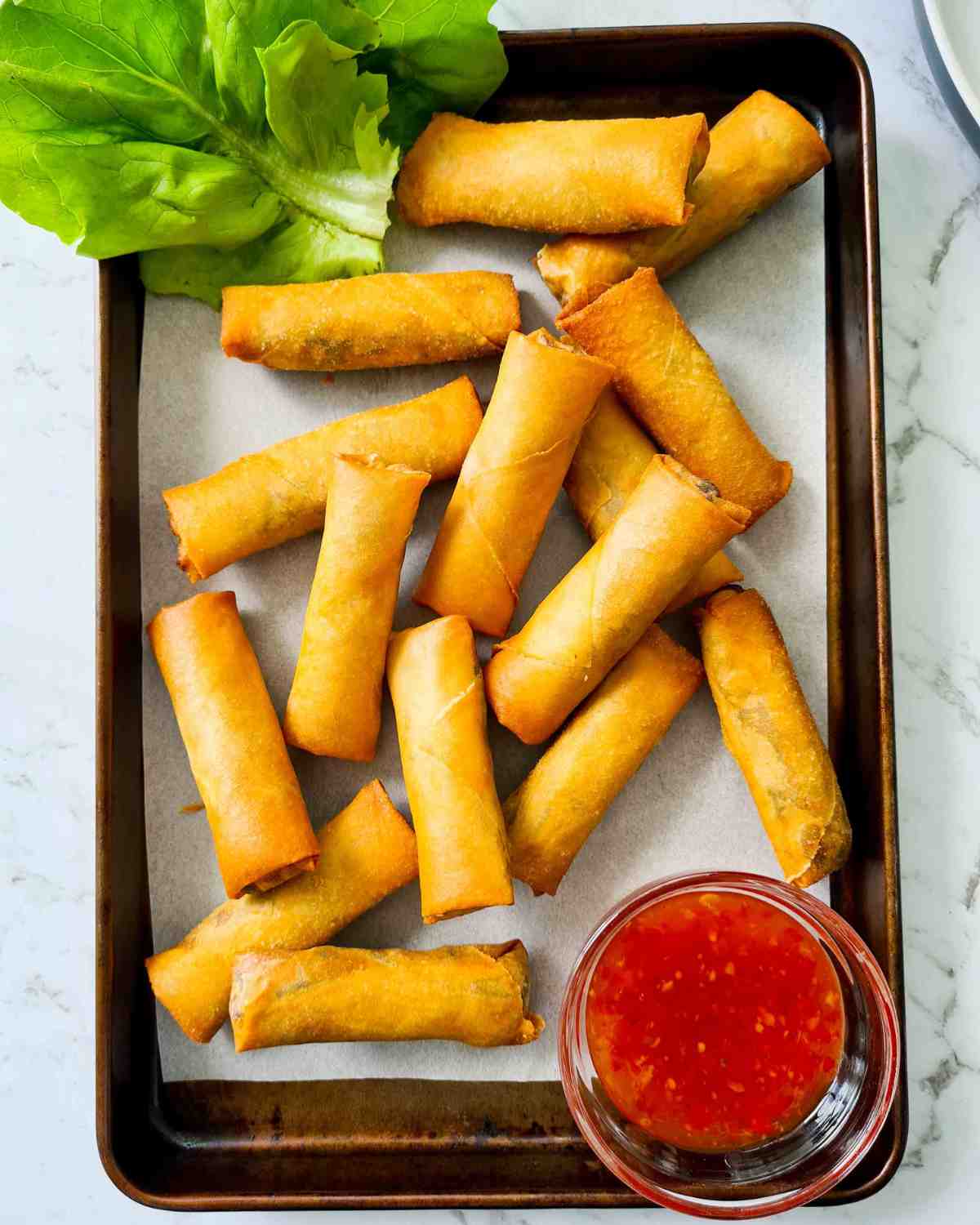 Crispy golden pastry rolls in a lined baking tray with a small bowl of sauce