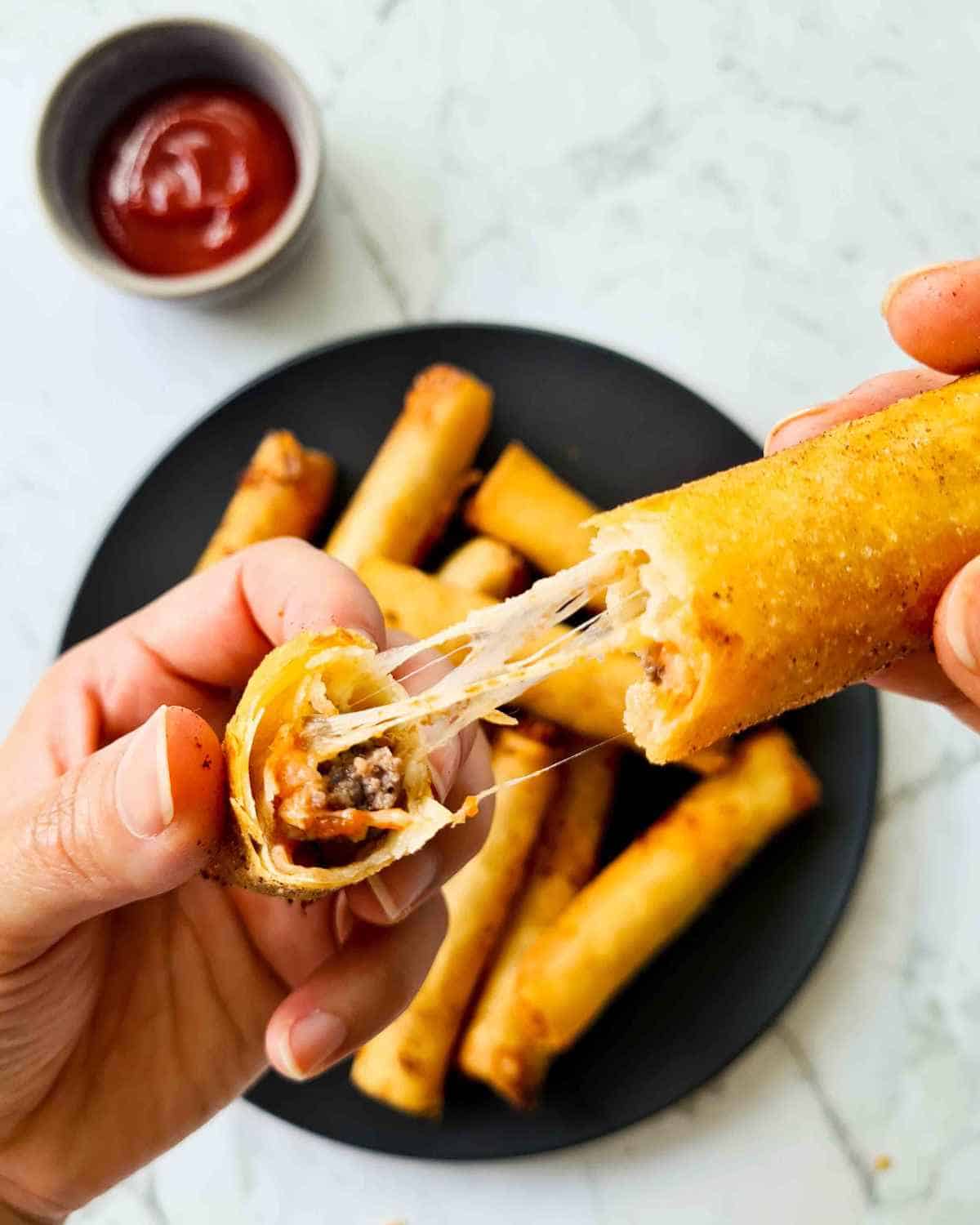 a cheeseburger spring roll broken in half by 2 hands showing the filling and pulled cheese