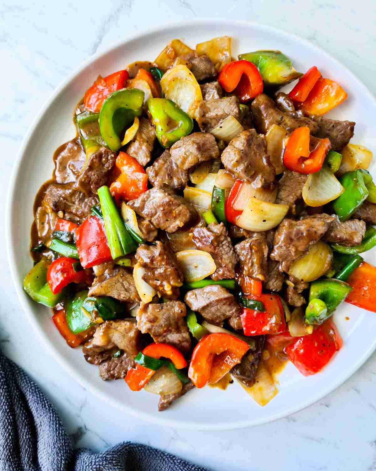 beef cubes and vegetables in a black pepper sauce on a round white plate