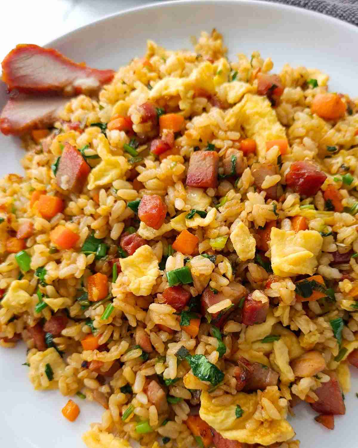A plate of fried rice with focus on BBQ pork pieces and golden eggs