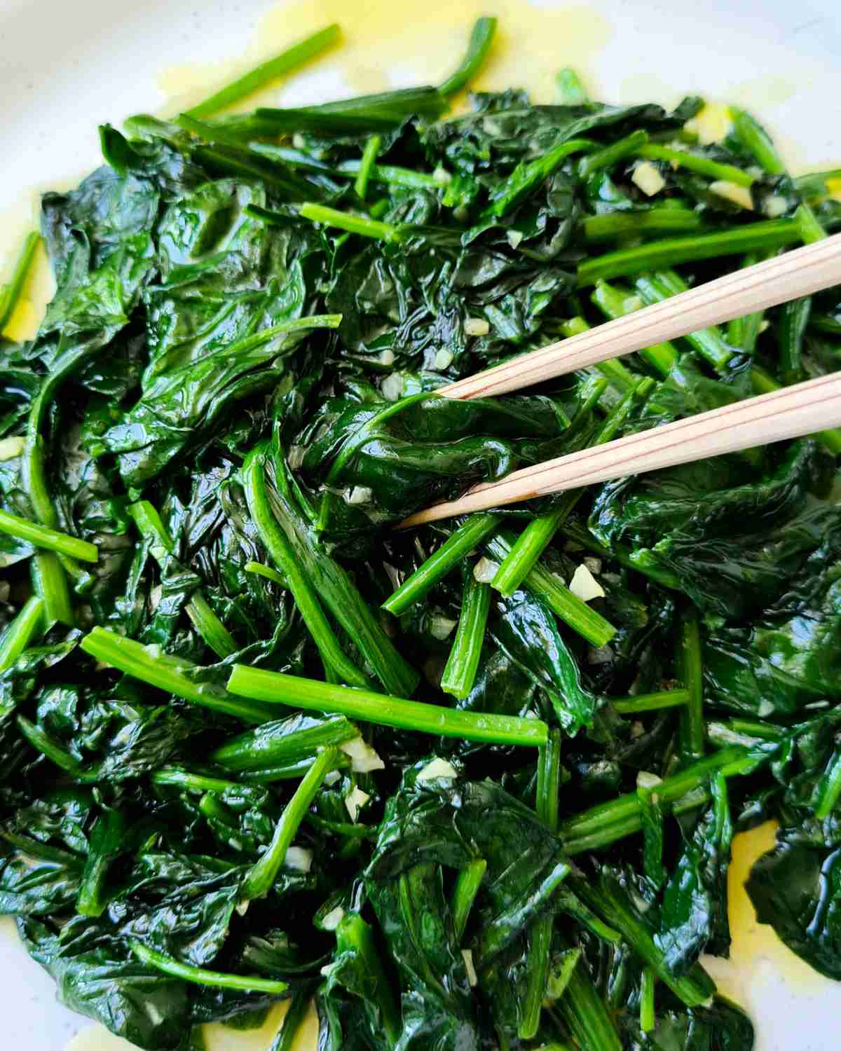 Close up of stir fried spinach with a pair of chopsticks picking up a piece