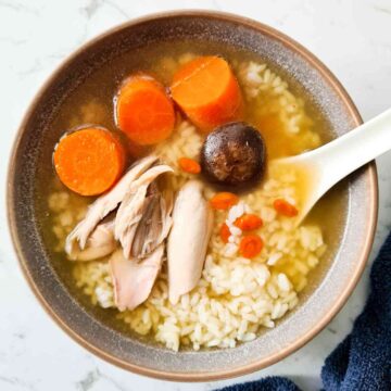 A bowl of clear chicken soup with carrots and rice