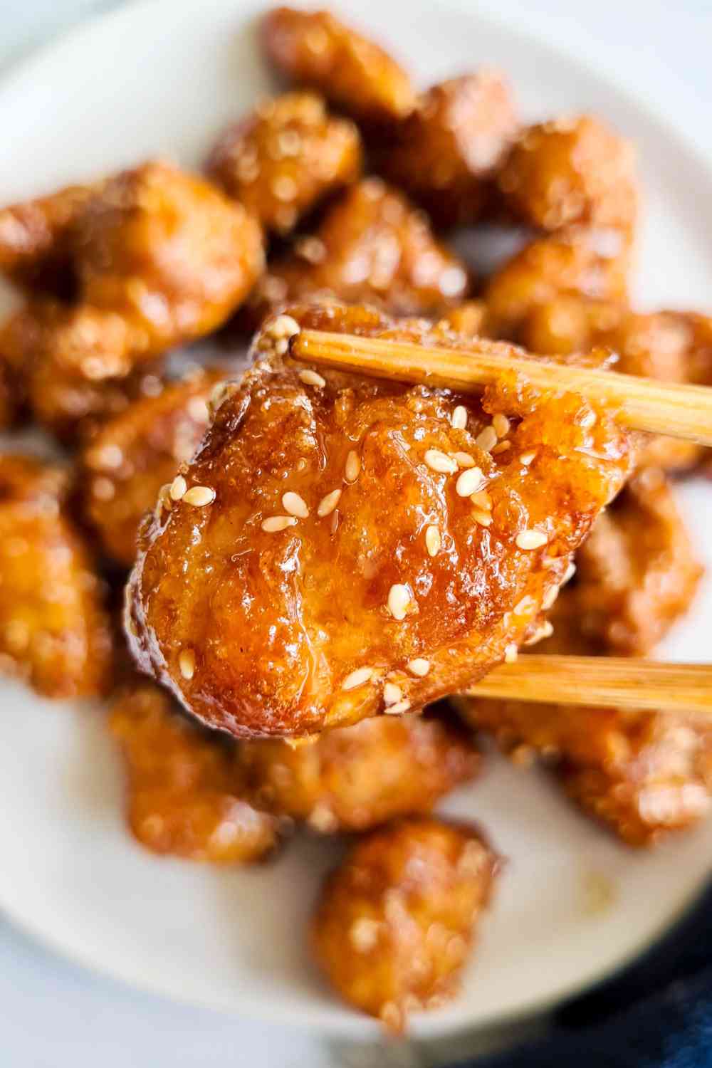 A piece of crispy chicken bite being held up of a pair of chopsticks