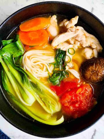 A bowl of clear noodle soup topped with vegetables and chicken