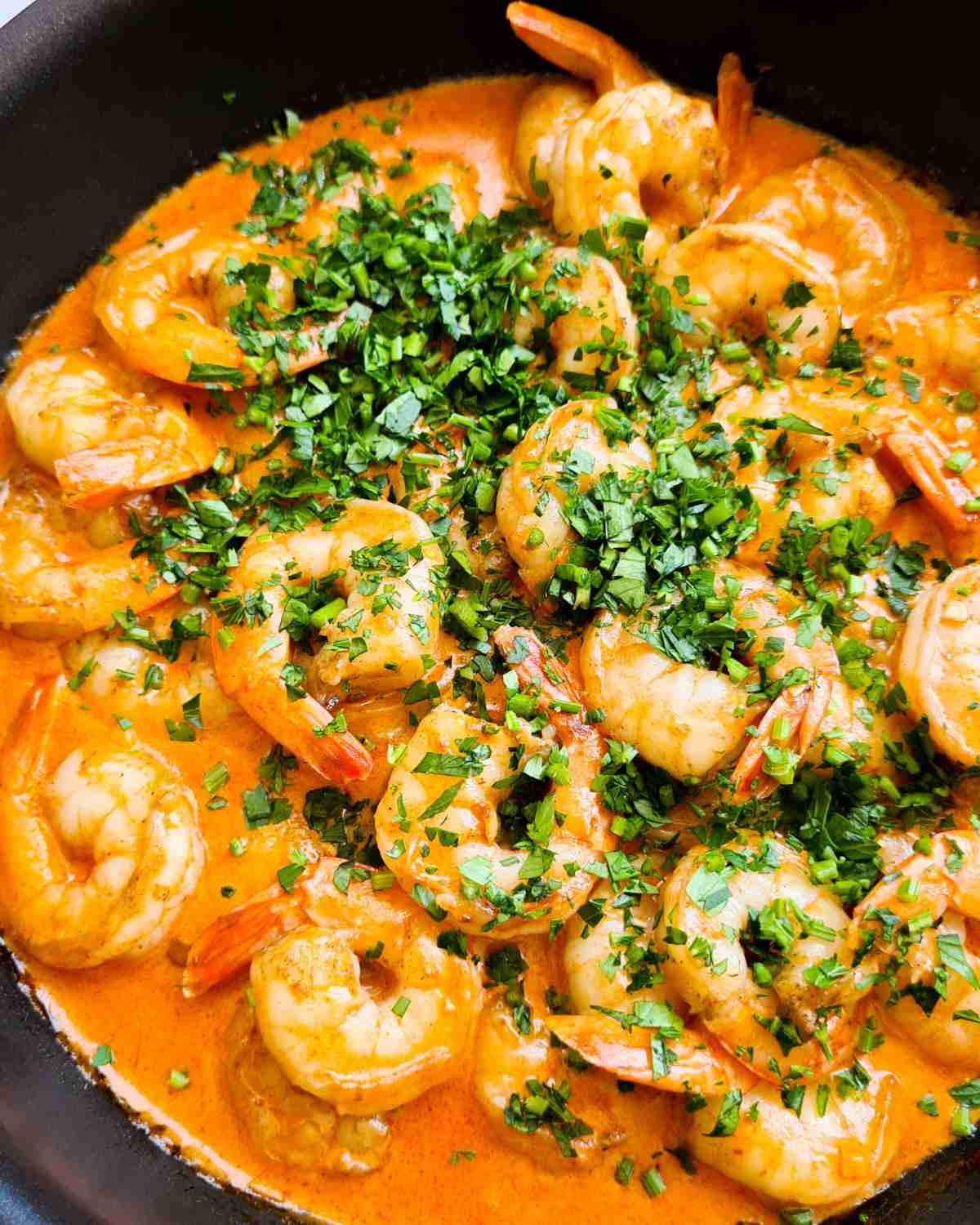 Creamy garlic shrimp (prawns) topped with finely chopped fresh parsley in a frying pan
