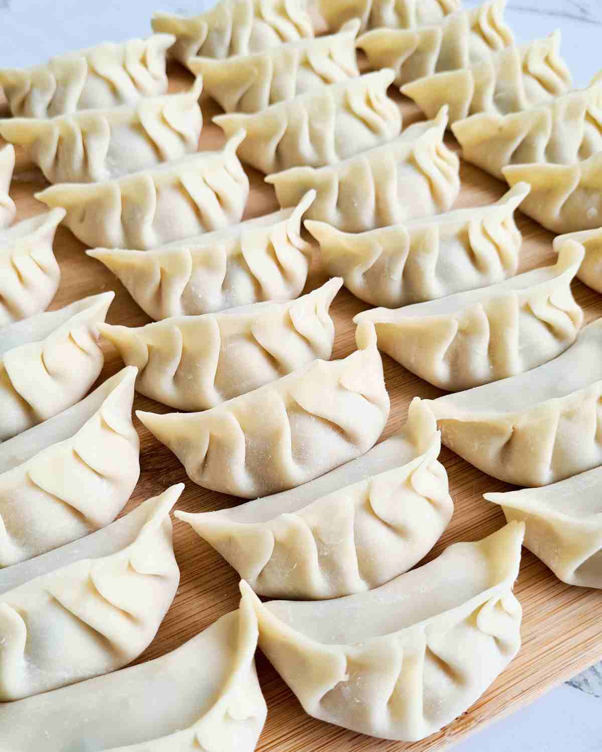 Rows of neatly wrapped dumplings on a wooden chopping board