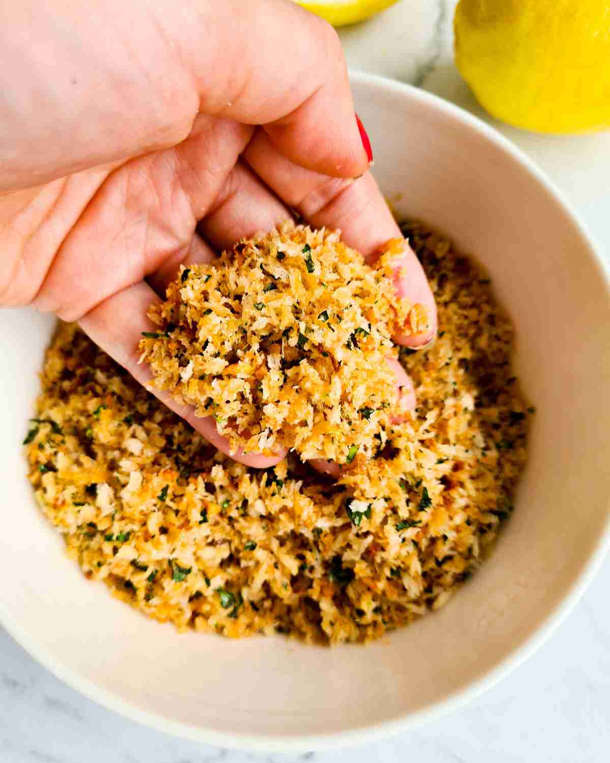 Golden herb breadcrumbs being scopped up by a hand over a bowl