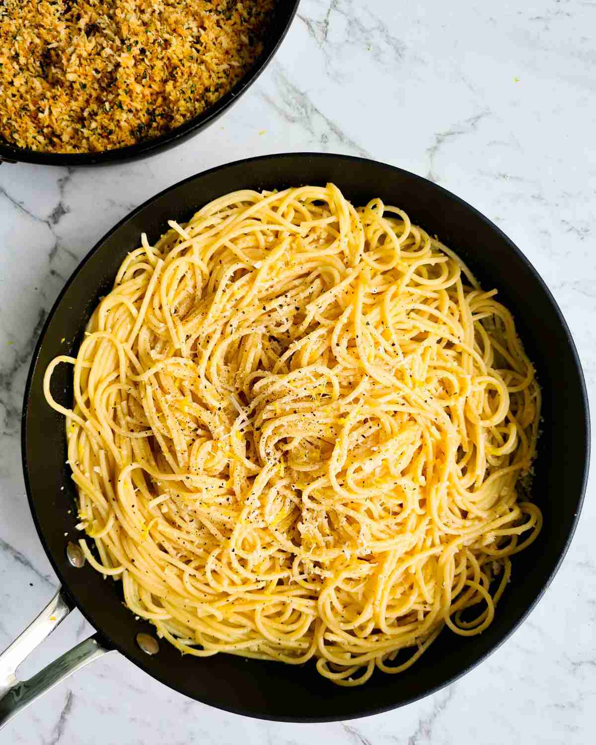 Spaghetti in a large frying pan with herbed breadcrumbs in the background